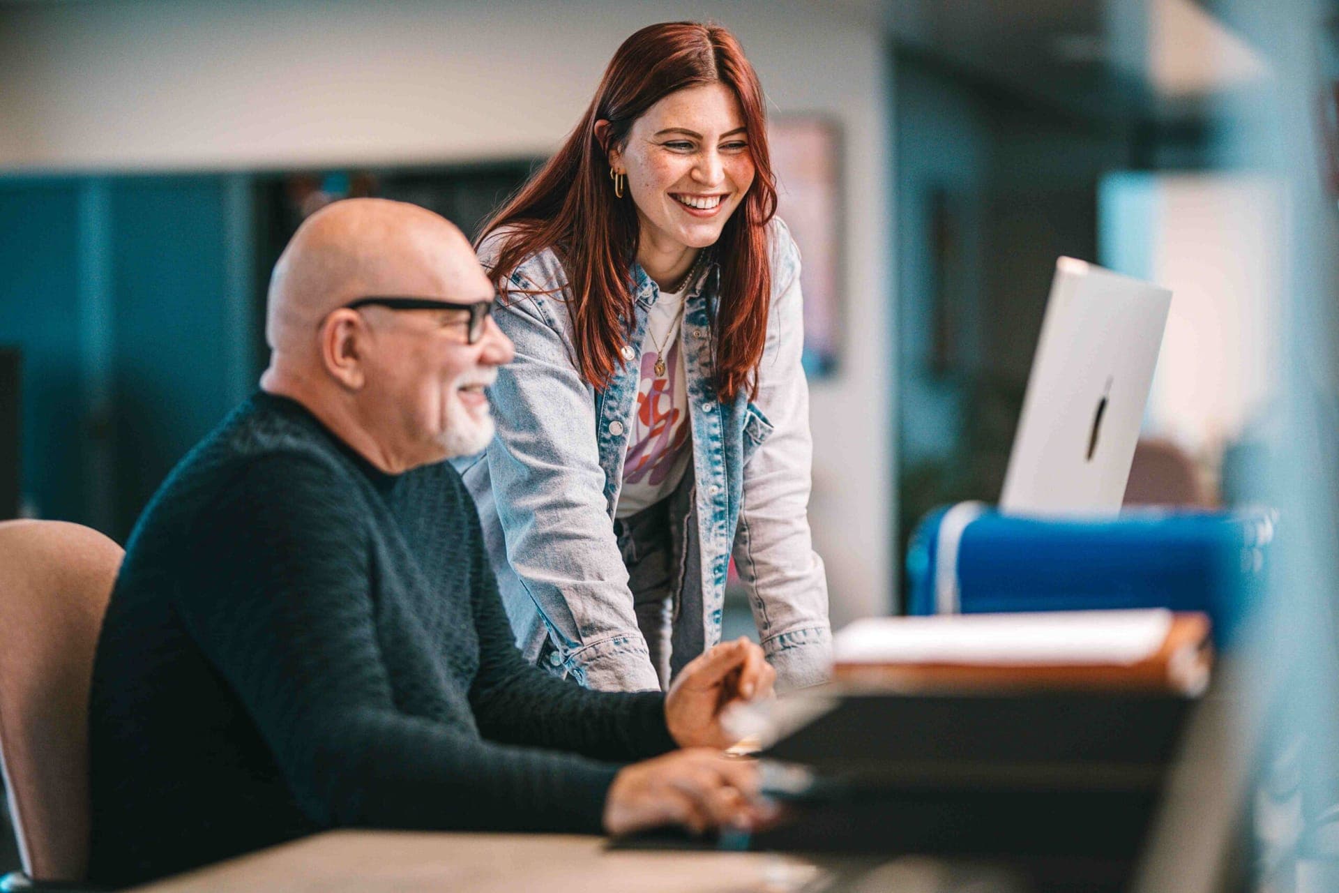 Twee collega's lachen samen aan een bureau terwijl ze achter een computer werken