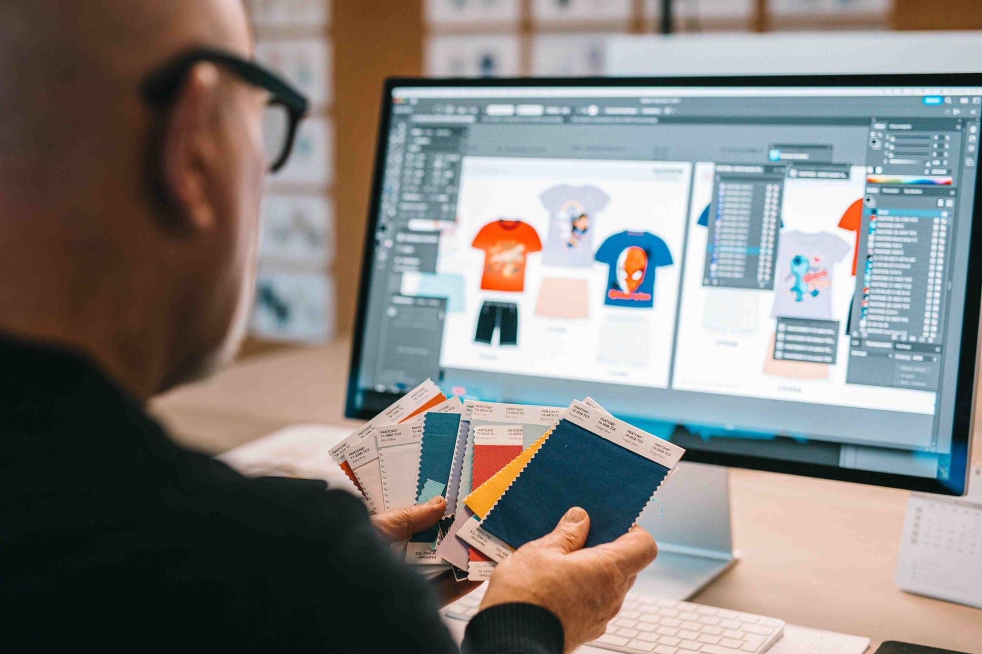 Ontwerper met Pantone-stofstaaltjes voor een scherm met ontwerpen van gelicentieerde kinder-t-shirts
