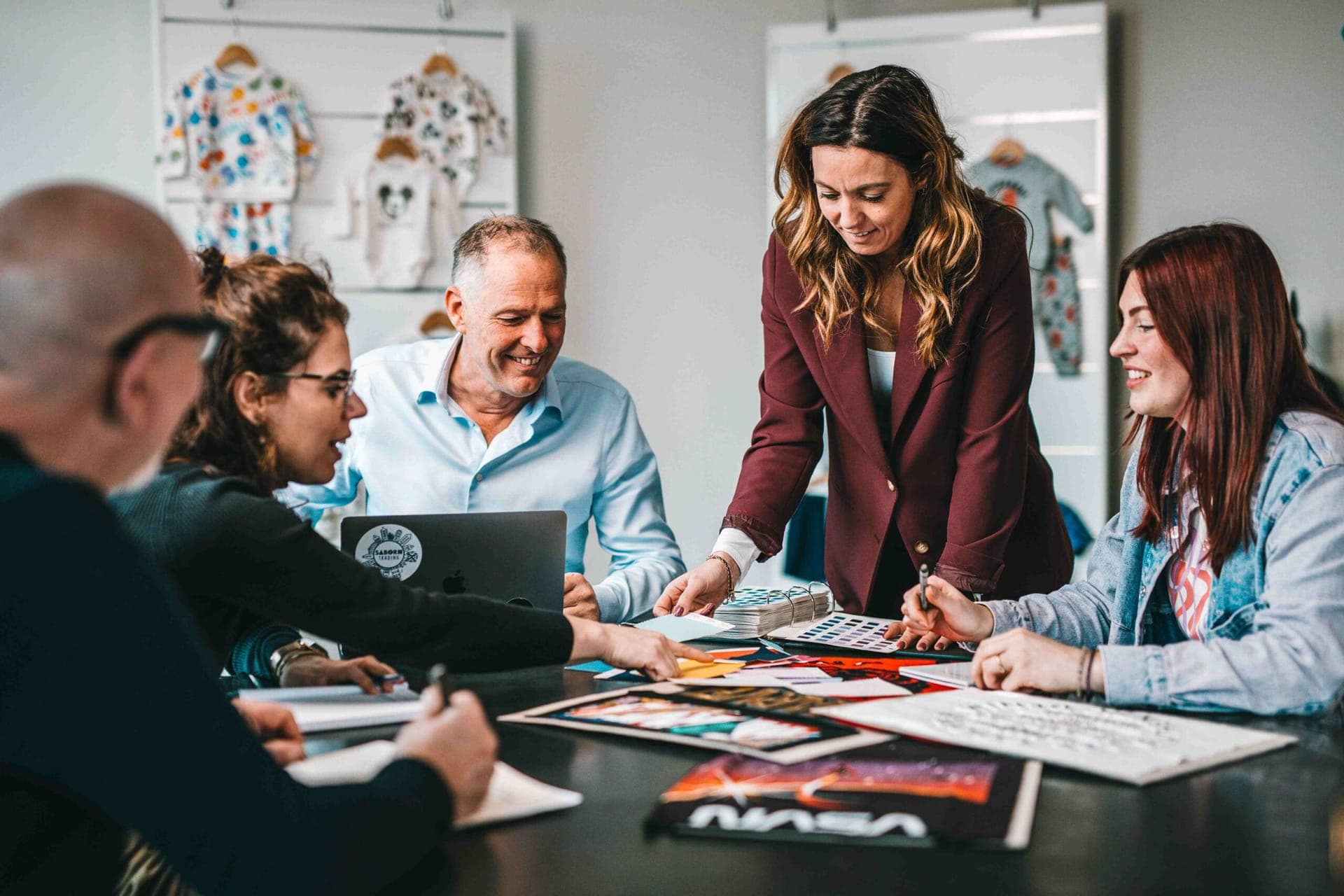 Team bespreekt kleuren en ontwerpen rond een tafel met stofstaaltjes en artwork van licentiegevers